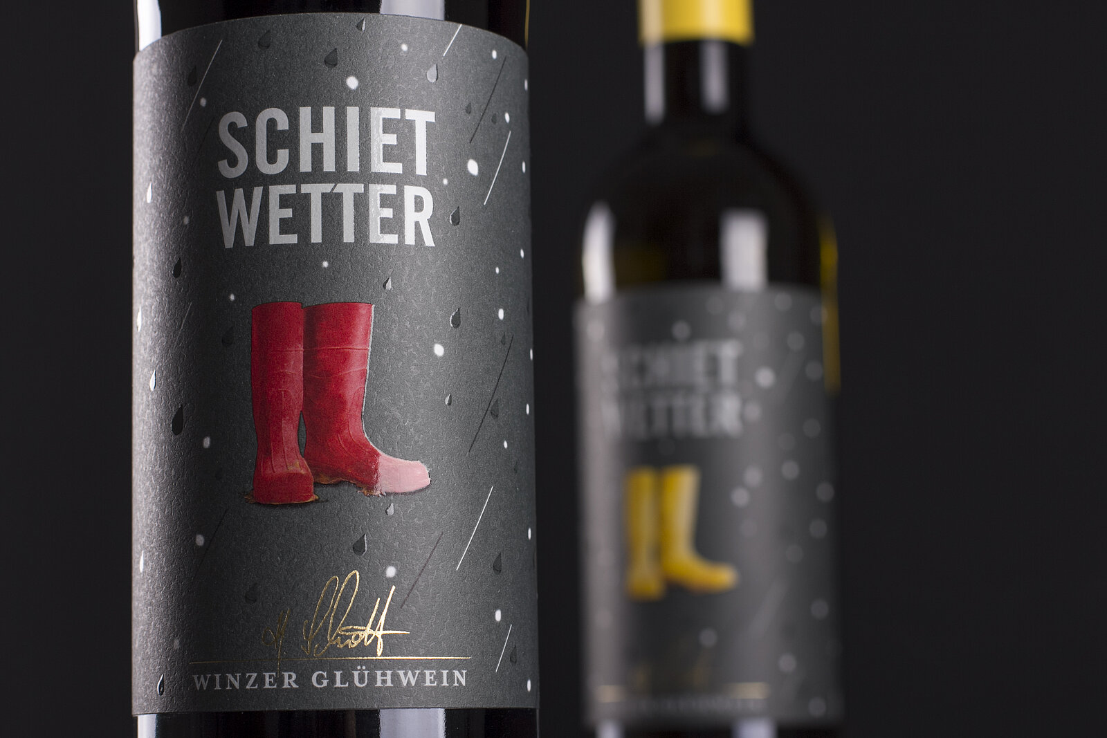 Weinetiketten vom Schietweter-Glühwein mit Gummistiefeln in Rot und Gelb. Die Etiketten sind veredelt mit Spotlack und Goldfolie.